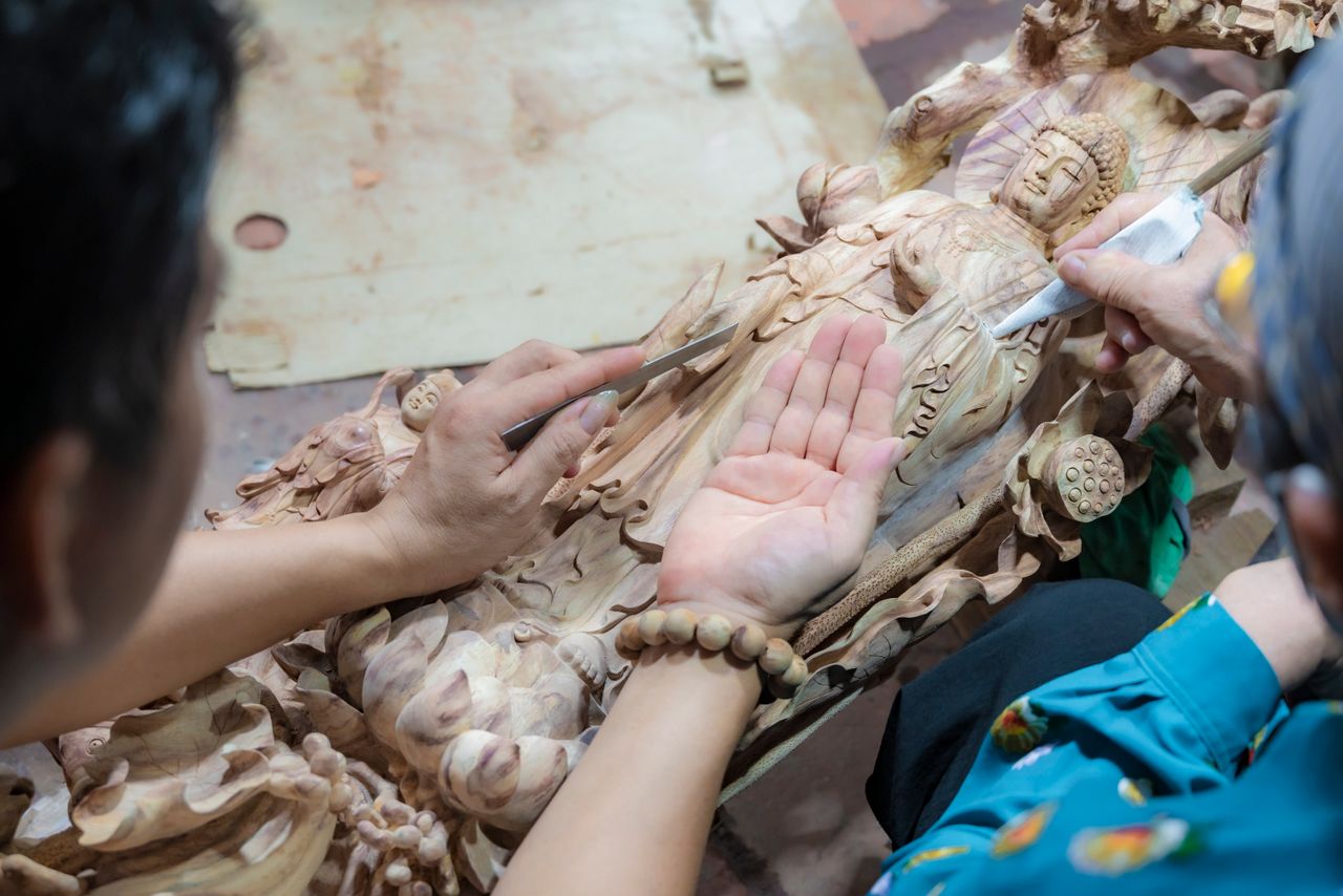 services-01 Close-up of artisans skillfully carving a wooden Buddha statue with intricate detail by hand.