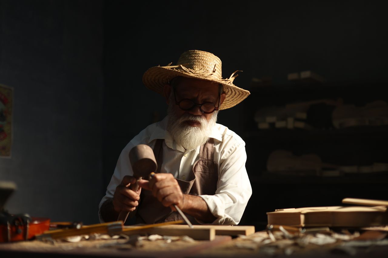 our-experience An elderly craftsman works meticulously in his workshop, carving wood with dedication.
